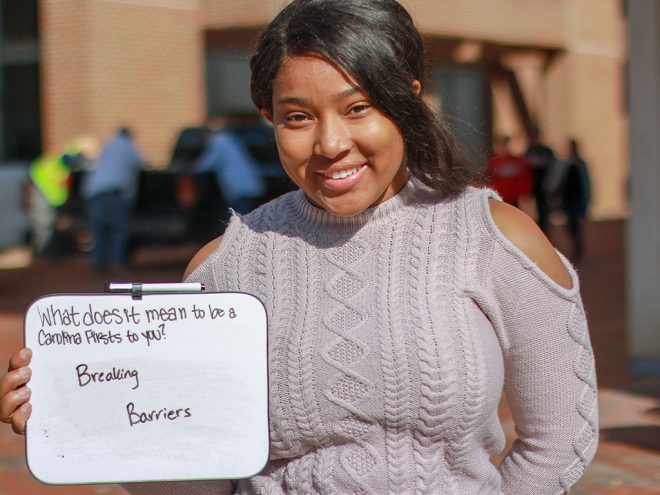 Jasmine Jackson holds a sign saying, "What does it mean to be a 'Carolina First' for you? Breaking Barriers".