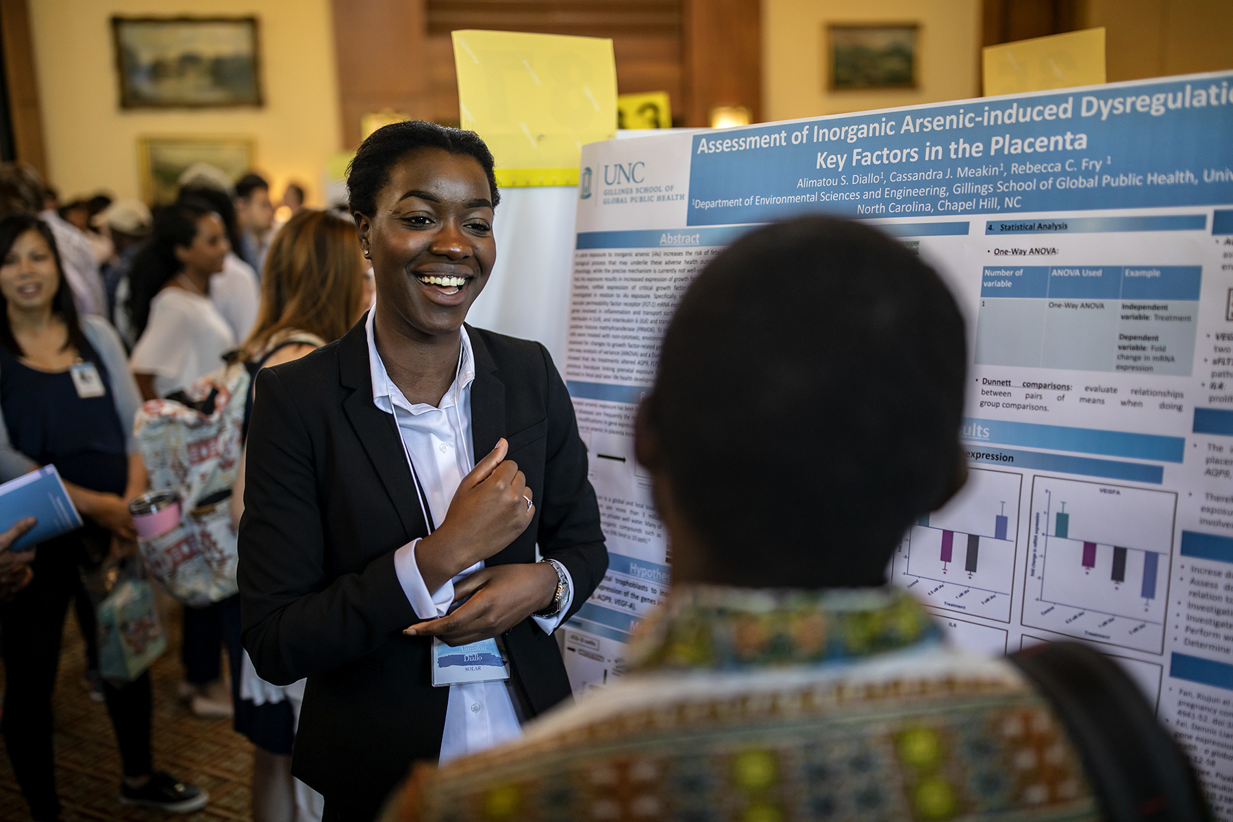A laughing woman stands before her research poster at the Summer Undergraduate Pipeline Research Symposium