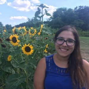 Natalia Rebolledo wearing a blue shirt and standing in a field of sunflowers.
