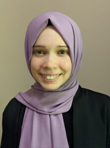 A woman in a purple hijab smiles.