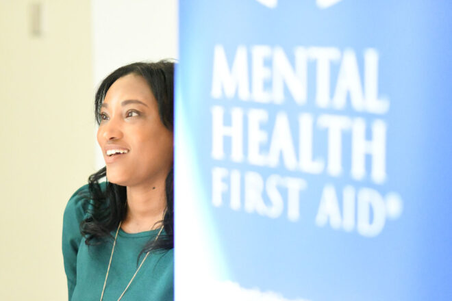 A woman poses beside a poster that reads mental health first aid
