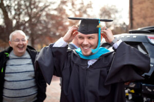 A person smiles while wearing doctoral regalia