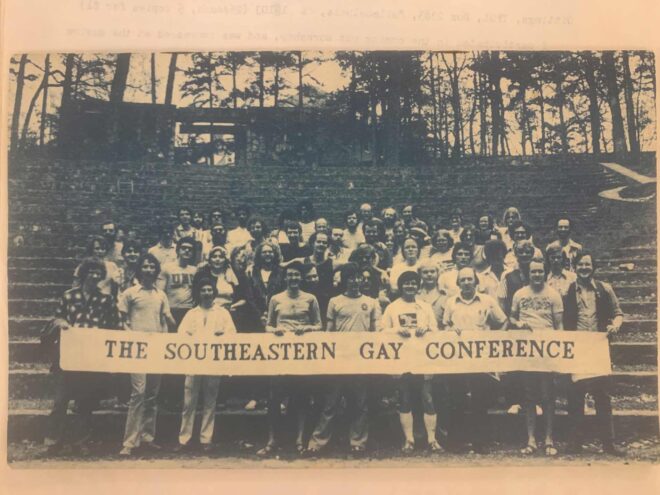A group of people standing at the bottom of stairs holding a banner that reads the southeaster gay conference. Black and white photo