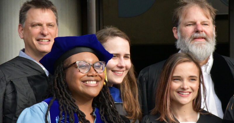 A group of people wearing doctoral regalia smile