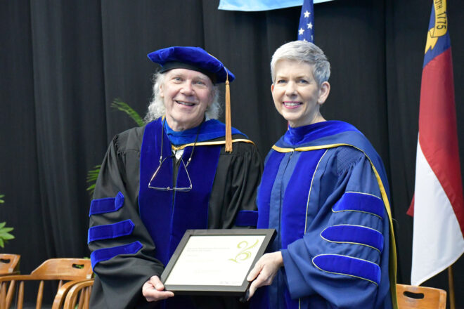 Two people stand in doctoral regalia