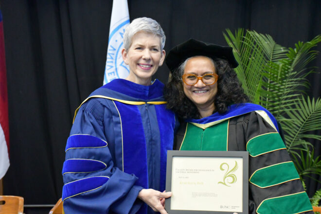 Two people stand in doctoral regalia