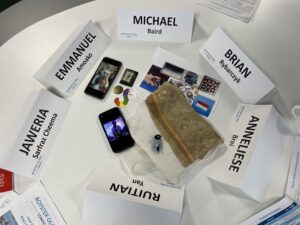 Six name tags placed on a table encircling a variety of personal items, including photos, jewelry and clothing.